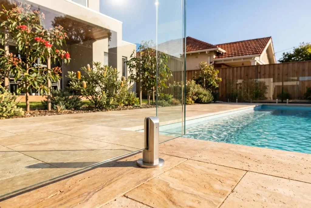 Frameless glass pool fence panel and stainless spigot detail on travertine paving in Northbridge
